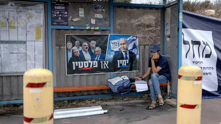 A young Israeli settler sits doing schoolwork at a bus stop adorned with election material for Prime Minister Benjamin Netanyahu's Likud party, outside the Palestinian village of Haris in the Israeli-occupied West Bank on October 26, 2026. Israel heads to the polls on October 27 in its first election since the October 7, 2023 Hamas-led attack, in what is seen as a referendum on the prime minister. (Photo by Ilia YEFIMOVICH / AFP)